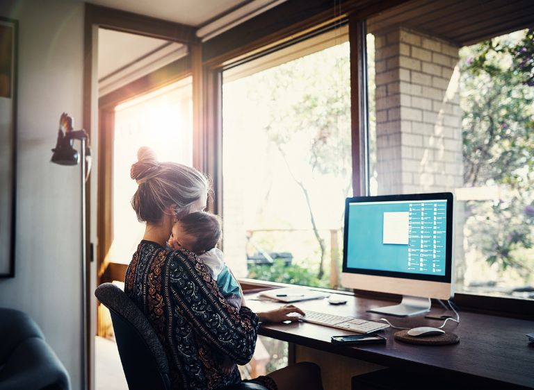 Income-contingent loans: A mother sits in front of a computer at home with her baby.