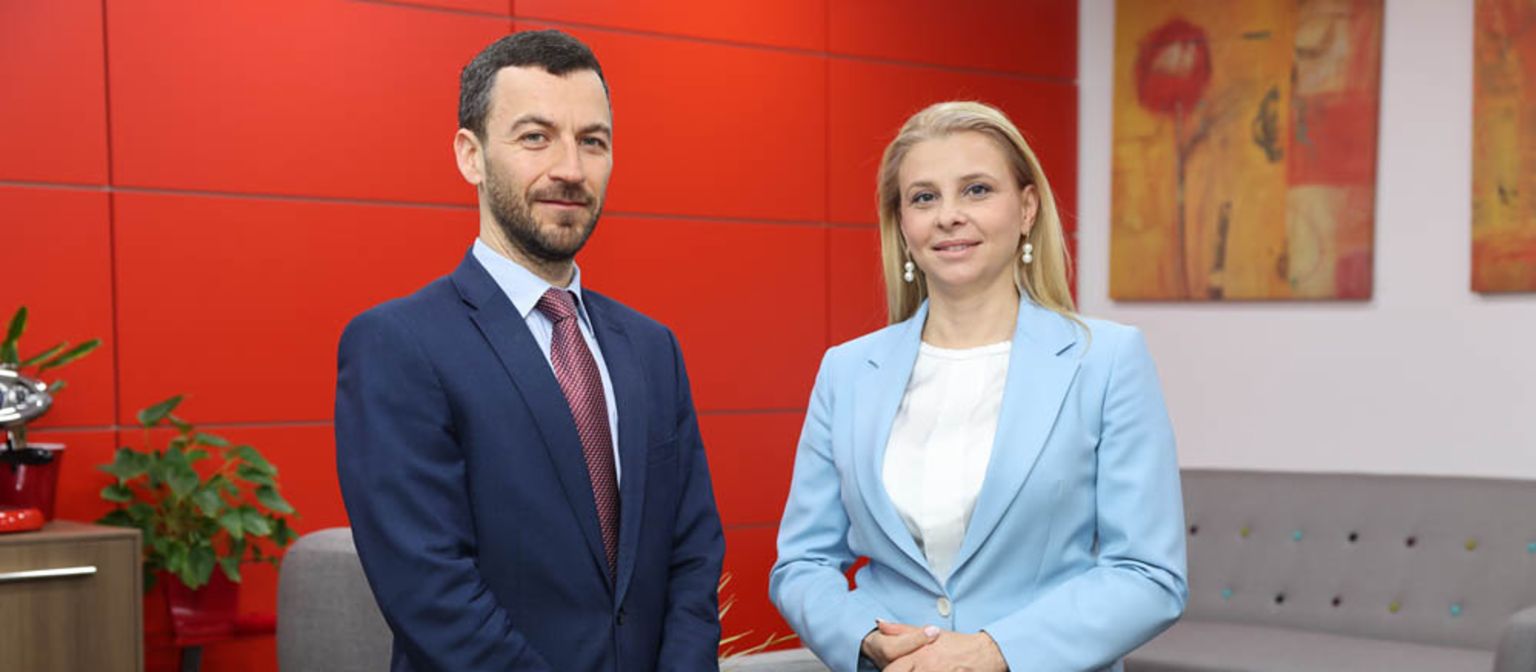 CEO Vladislav Hadjidinev in a blue suit and Katerina Bosevska Managing Director of EOS North Macedonia in a light blue blazer standing next to each other in a office with a red wall