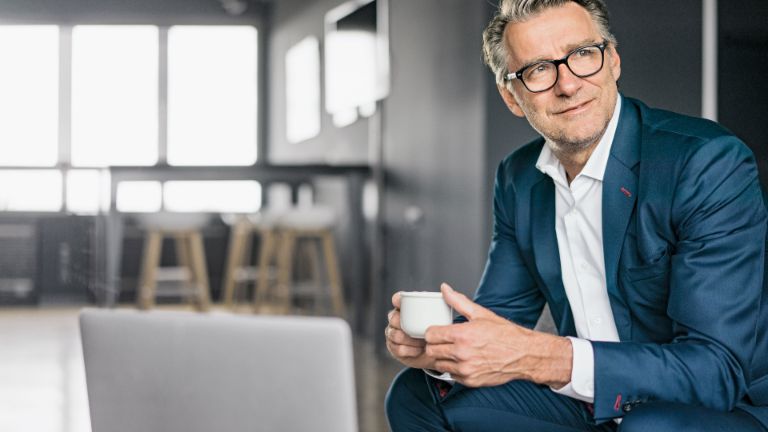Portrait of a sitting mature businessman wearing a blue suit holding a white coffe cup
