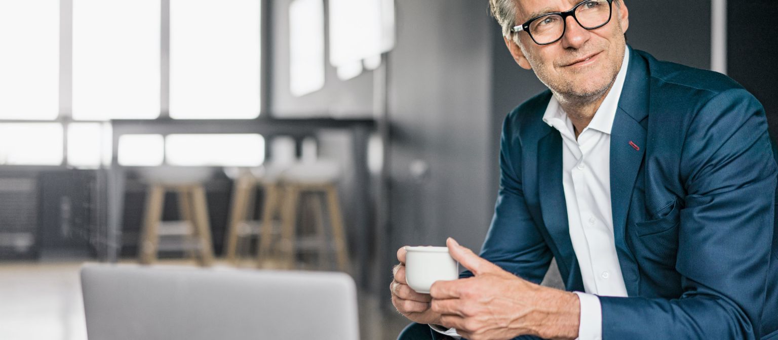 Portrait d'un homme d'affaires mûr assis, portant un costume bleu et tenant une tasse de café blanche