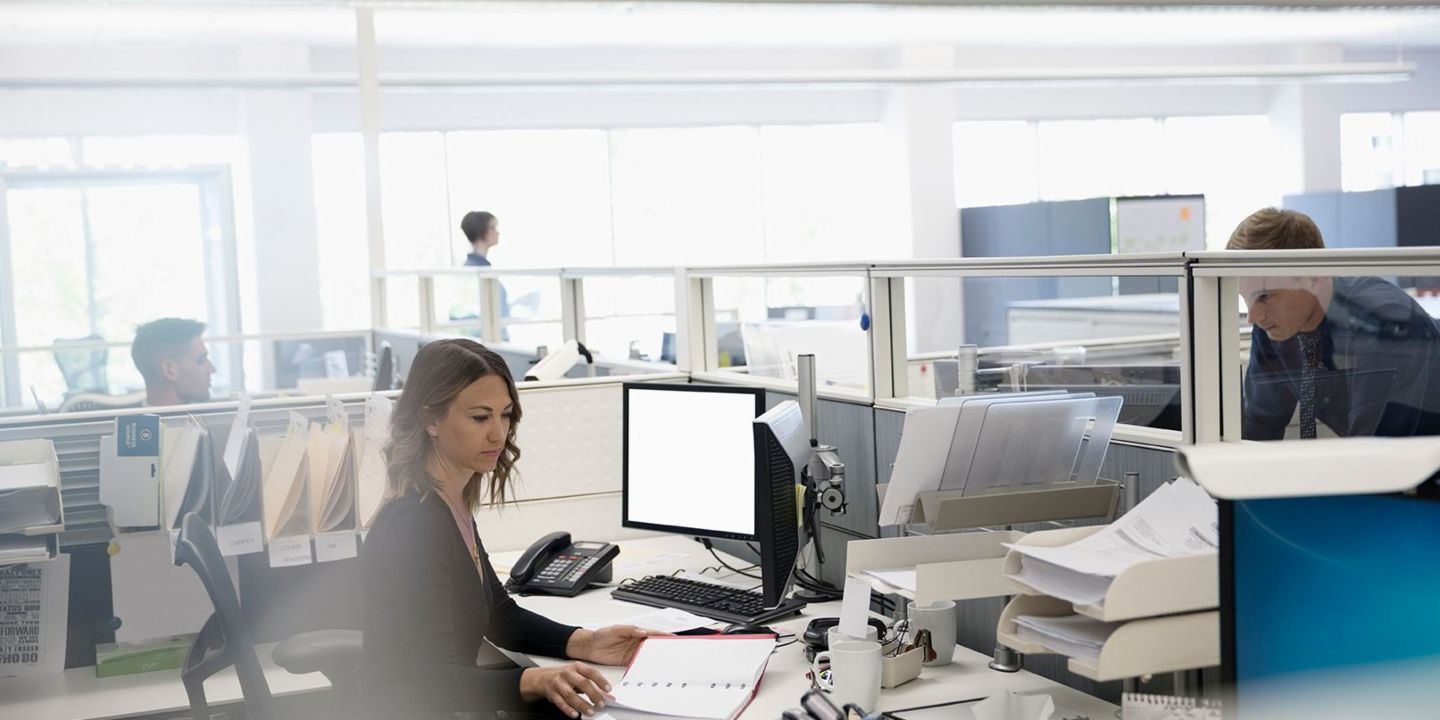 Numérisation: trois employés se trouvent dans un bureau open space, une femme est assise entre des papiers et son ordinateur
