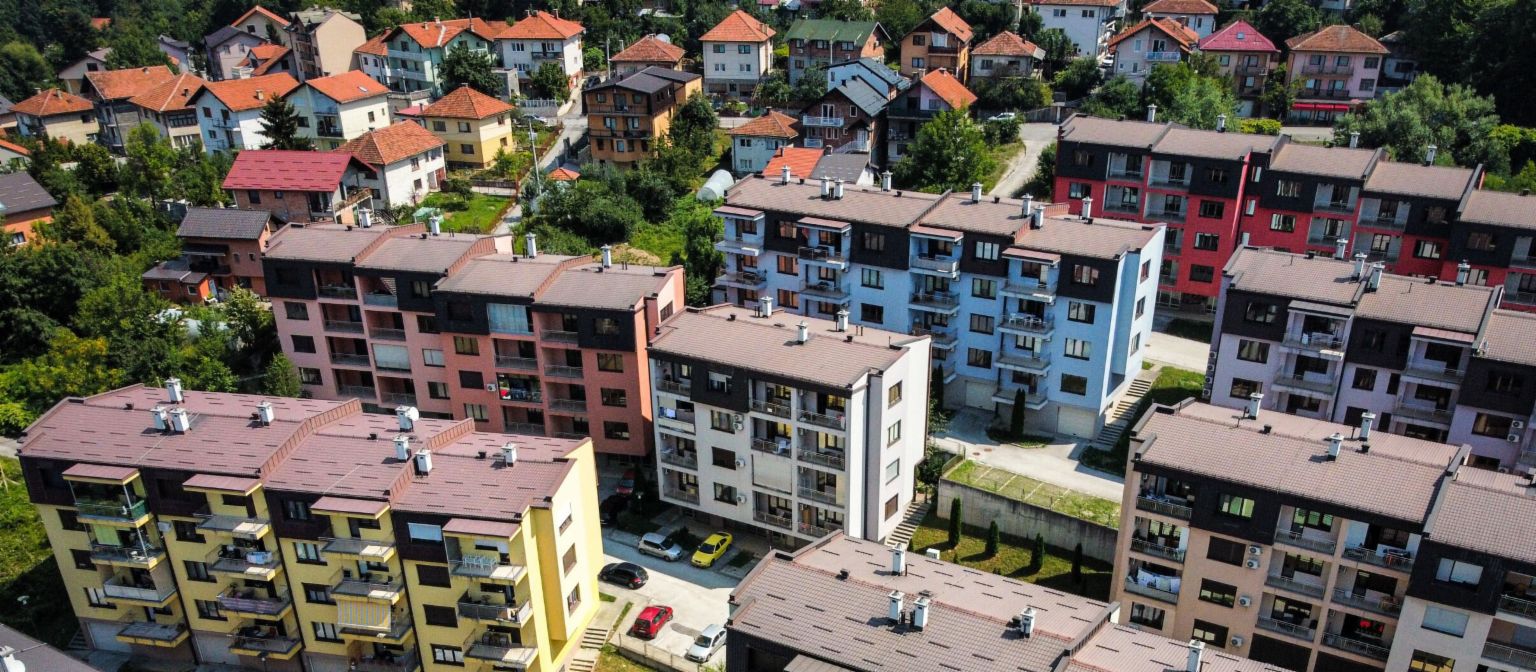 An aerial view highlights a vibrant residential complex featuring numerous multi-colored apartment buildings amidst green surroundings in Bosnia.