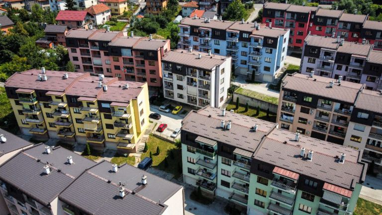 An aerial view highlights a vibrant residential complex featuring numerous multi-colored apartment buildings amidst green surroundings in Bosnia.