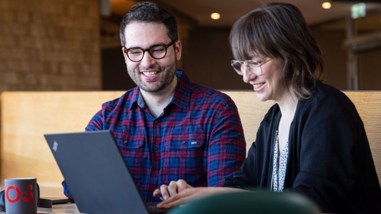 Two EOS employees look at a laptop together while engrossed in a conversation.