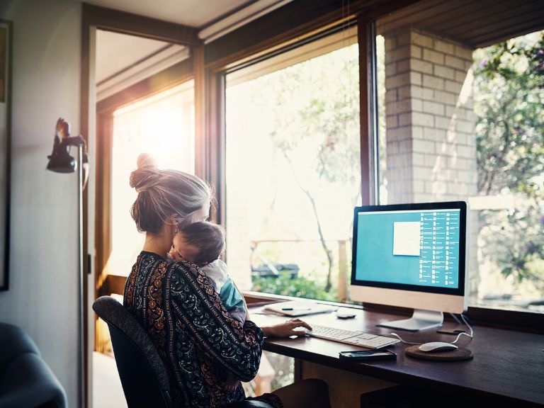 Income-contingent loans: A mother sits in front of a computer at home with her baby.