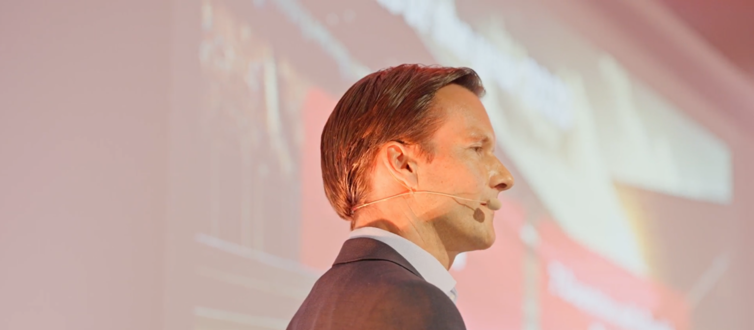 Profile shot of Carsten Tidow, Member of the EOS Group’s Board of Directors and responsible for Eastern Europe, on stage with a microphone and looking to the right. 