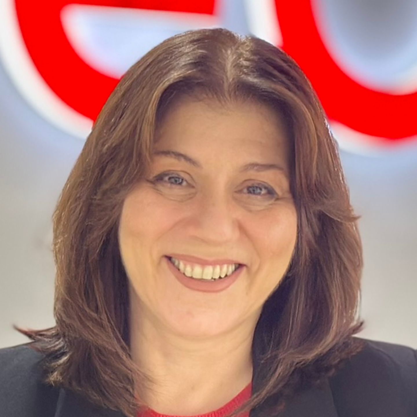 Belén Barreiro, agent Contact Center la EOS din Spania, stă sprijinită de un tejghea într-un blazer negru în fața unei sigle EOS strălucitoare.